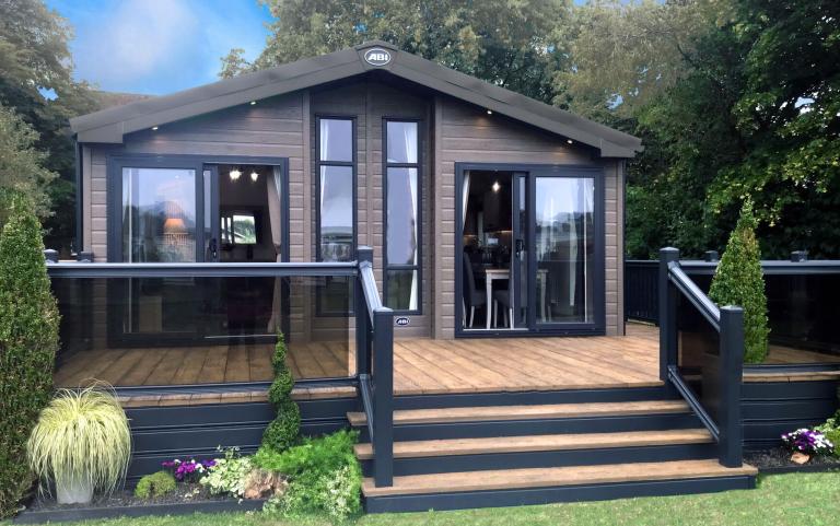 Outside View of a Luxury Lodge with a Decking area surrounded by Trees